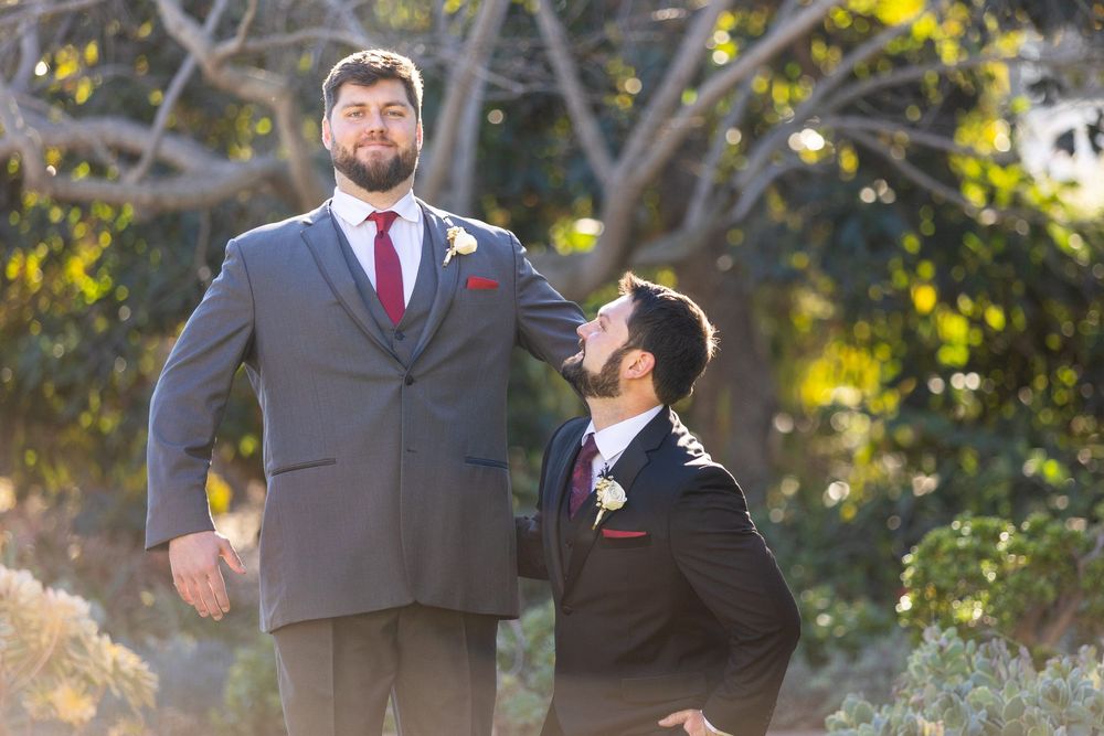 Groomsmen in gray suits and burgundy ties pose outdoors during a fall wedding celebration.