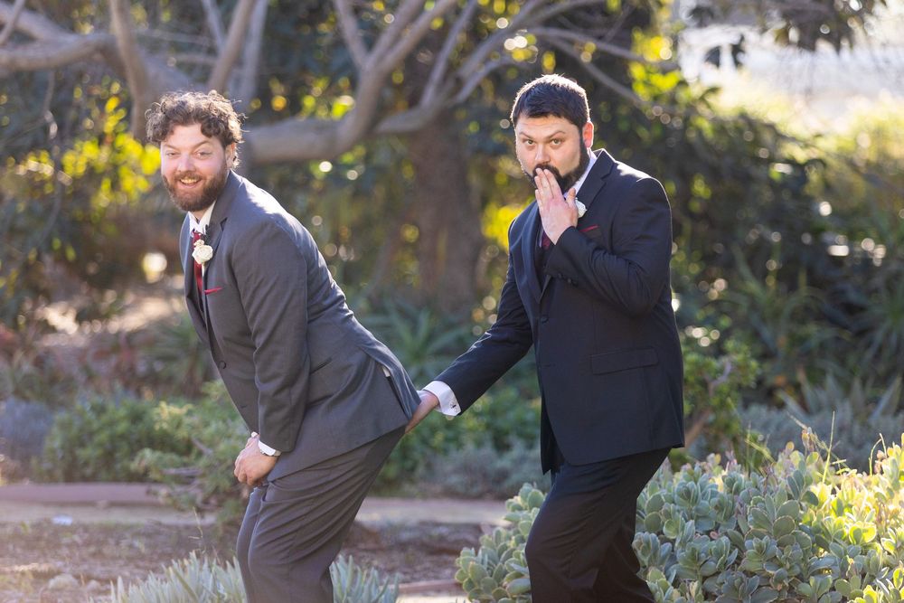 Two groomsmen in suits strike playful poses in an outdoor garden setting.