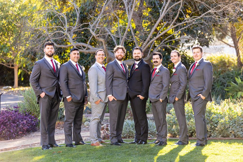 Wedding party in gray suits poses together outdoors on a sunny autumn day in a garden setting.