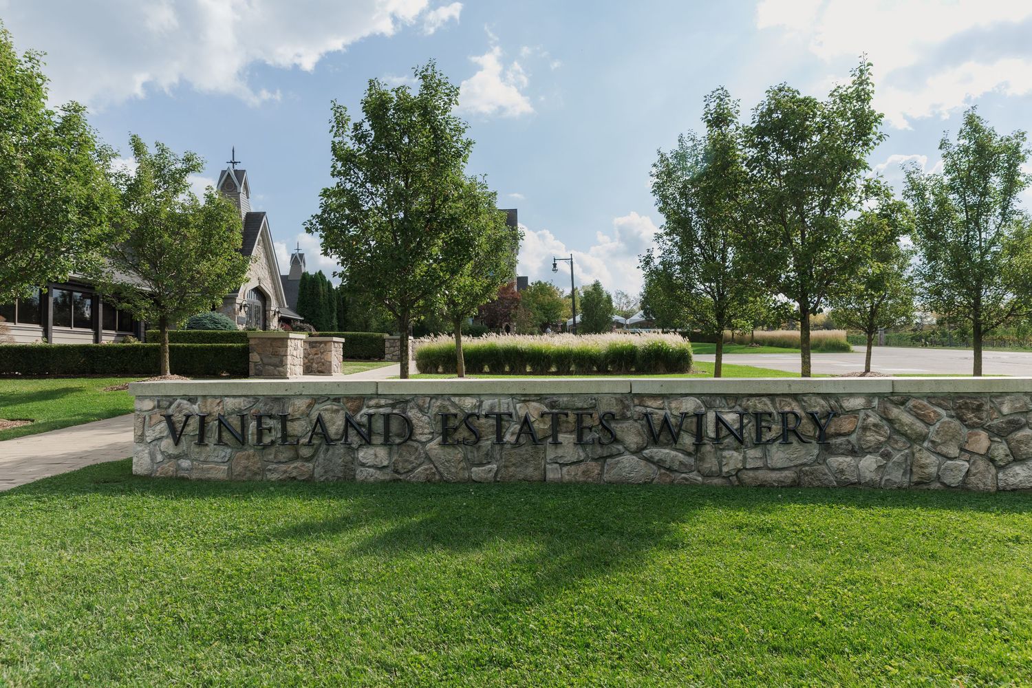Stone entrance sign for Vineland Estates Winery surrounded by manicured lawn and trees.