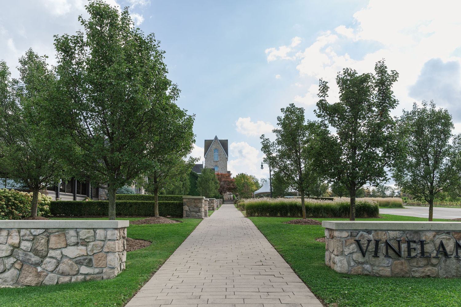Long stone pathway leading to Vineland Estates with stone walls and trees lining the entrance at Vineland Estates Winery.