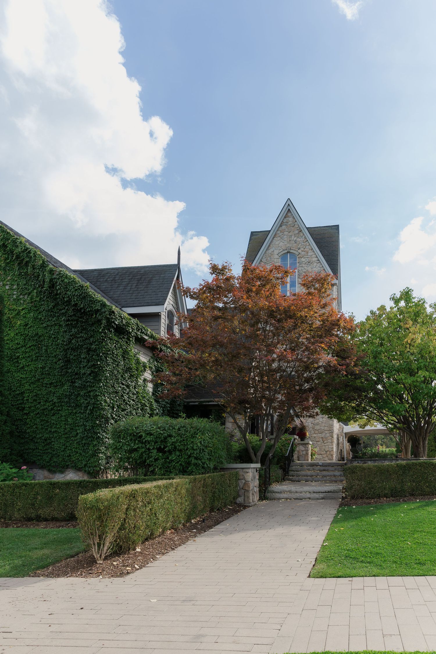 Ivy-covered stone building with steep rooflines and manicured hedges along walkway at Vineland Estates Winery.