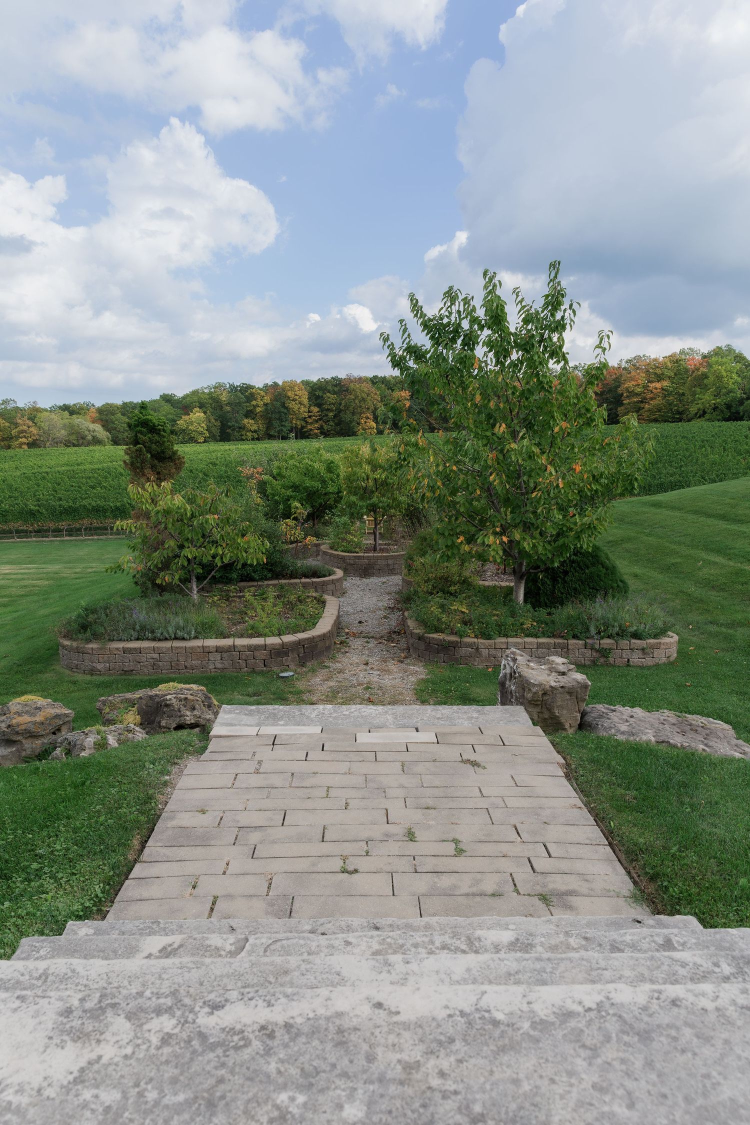 Stone-lined garden path leading through manicured grounds with trees and rolling vineyards at Vineland Estates Winery.