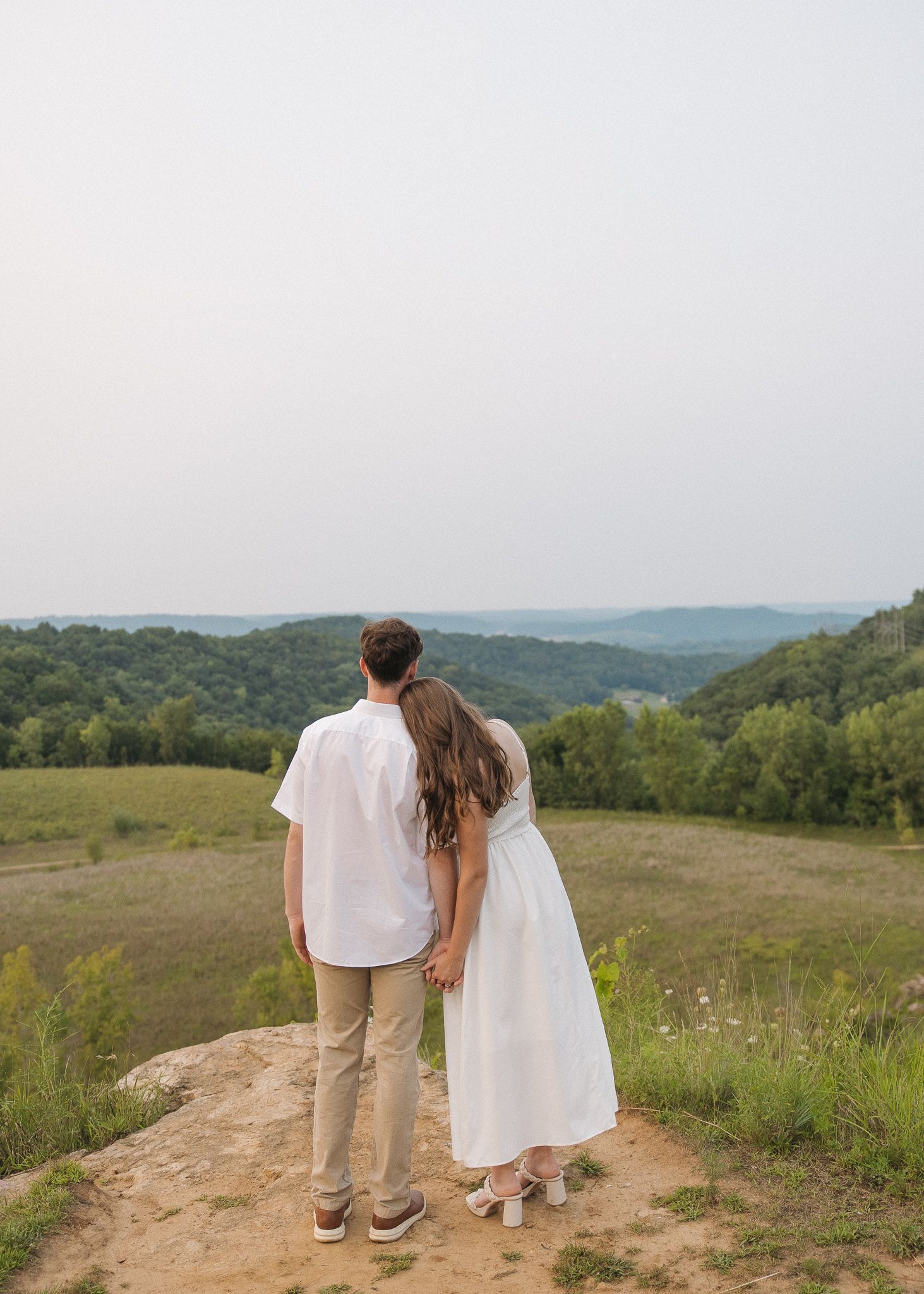 Close-up of couple holding hands while exchanging vows outdoors, with soft golden light filtering through trees.