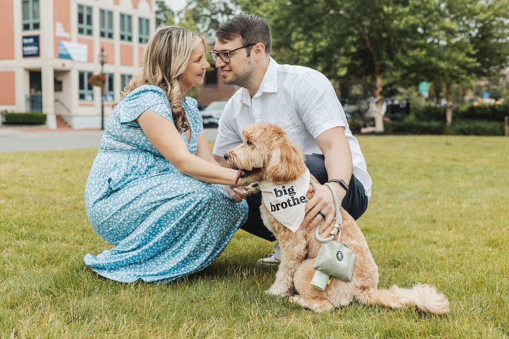 A couple in blue and white outfits plays with their golden retriever dog on a sunny lawn.