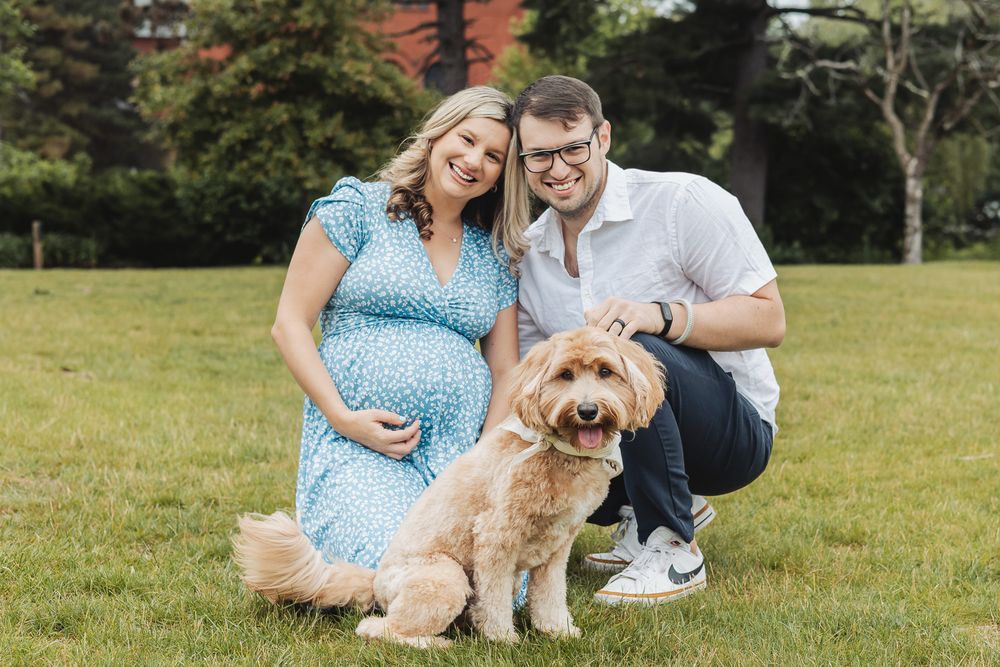 A couple in blue and white outfits poses outdoors with their golden retriever dog in a grassy field.