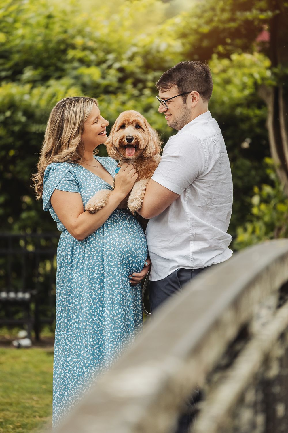 A couple in a garden shares joyful moments with their golden-colored dog on a sunny afternoon.