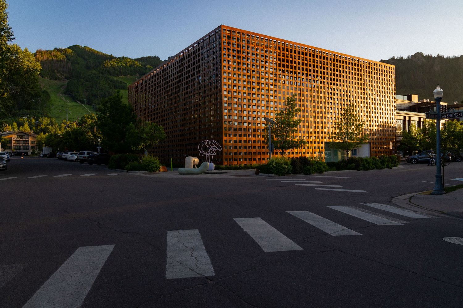 Modern building with distinctive terracotta-colored lattice facade illuminated at dusk in an urban setting with mountains behind.