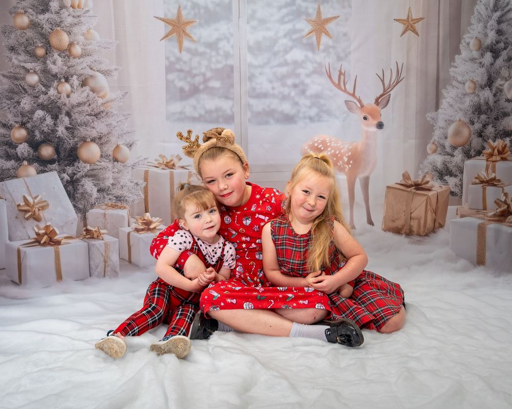 A winter holiday photo session with red and plaid outfits against a snowy backdrop with reindeer and star decorations.