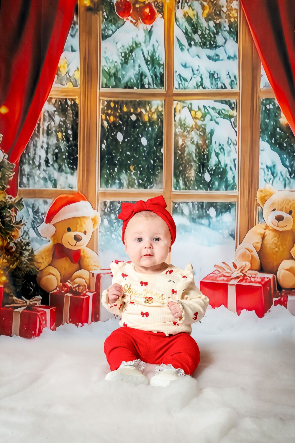 A festive Christmas scene with teddy bears, red bows, and gifts arranged on white snow by a window.
