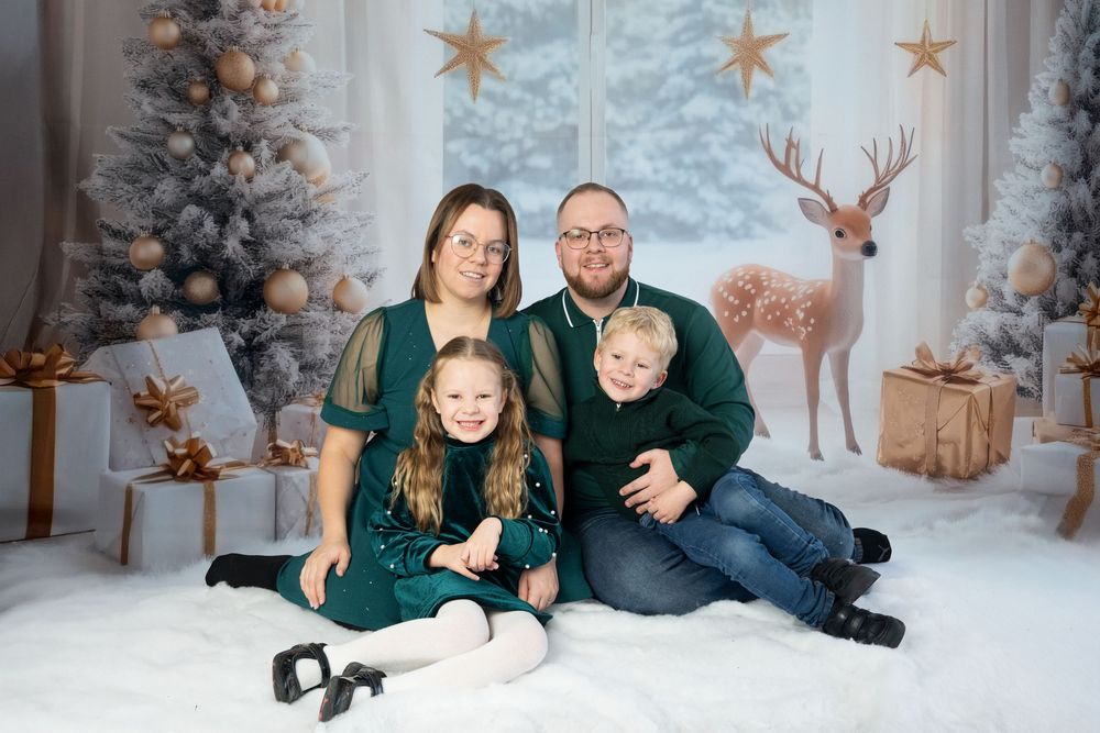 A family wearing green and black sits together in a winter wonderland themed photo studio setting with snow and reindeer decor.