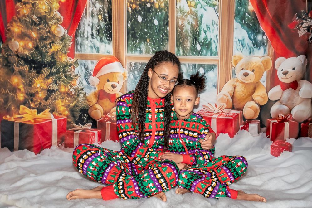 A festive holiday scene with matching Christmas pajamas, decorated tree, wrapped presents and plush toys by the window.