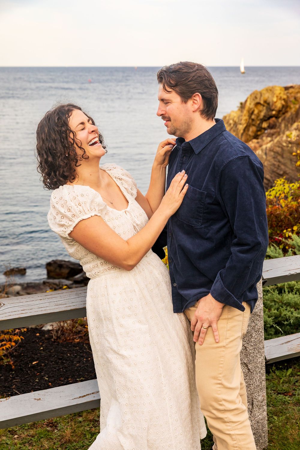 A couple shares romantic moments by the ocean during a coastal photoshoot at sunset.