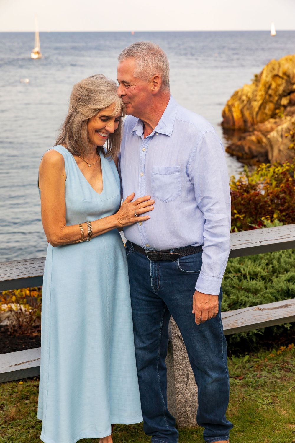 Couple in light blue and white outfits share an intimate moment by the ocean.
