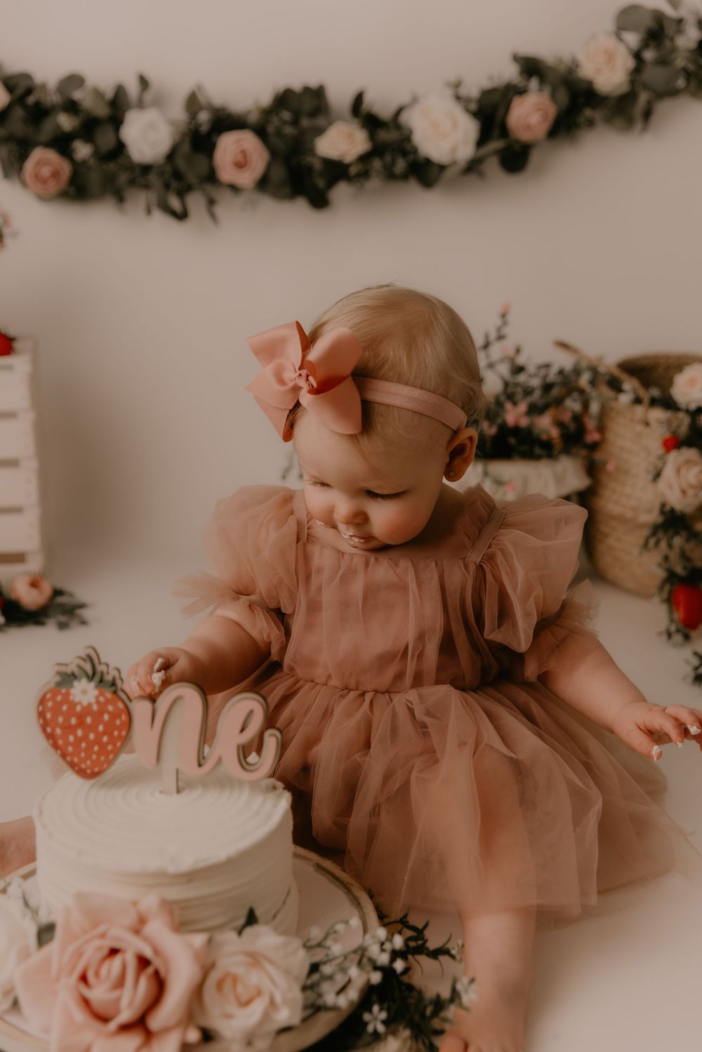Baby in a soft brown tulle dress poses against floral backdrop in vintage-toned nursery photography session.