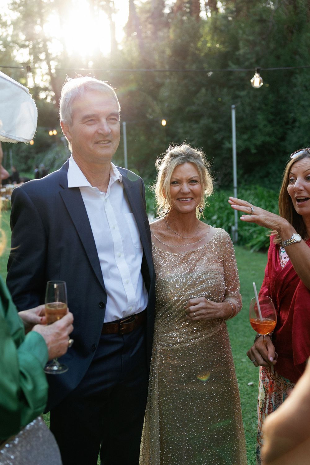 Elegantly dressed guests celebrate at an outdoor evening party with drinks and laughter.