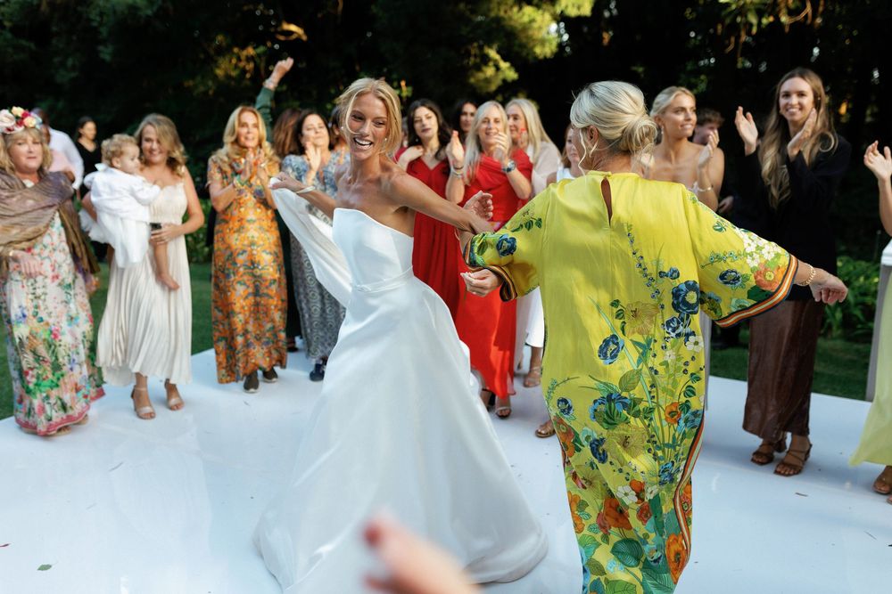 A group of wedding guests dancing and celebrating together on a white dance floor at an outdoor reception.