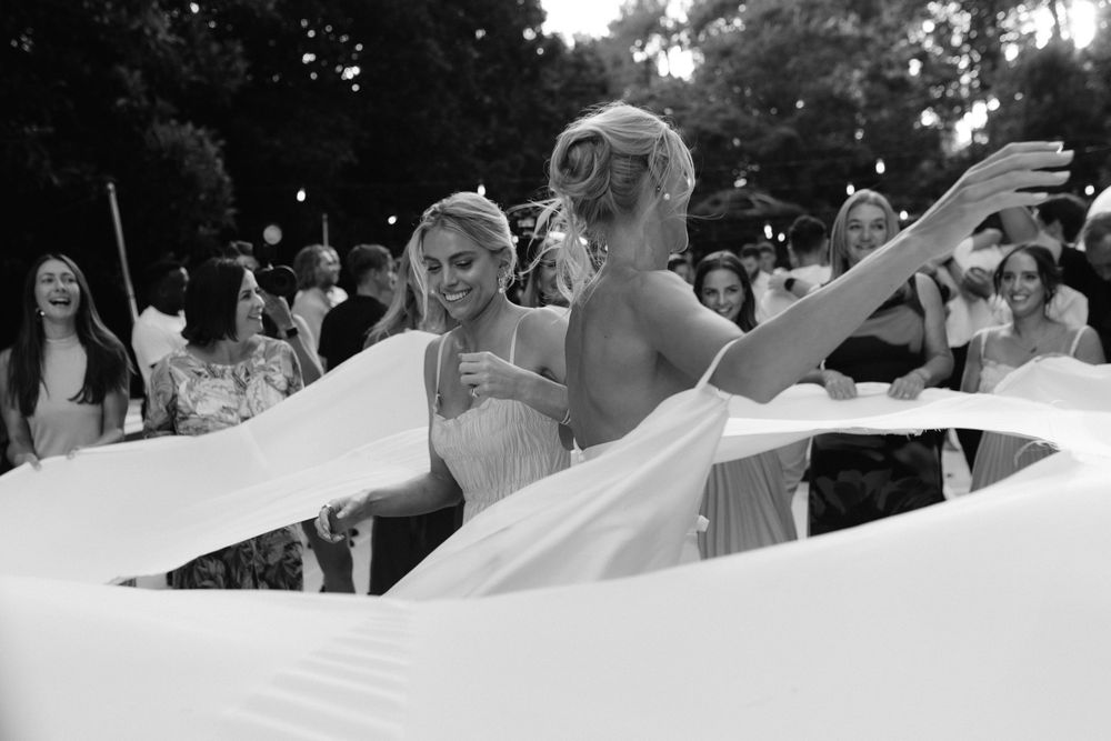 Wedding guests hold up a long white veil in an outdoor garden setting during a celebratory moment.