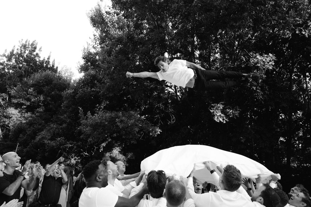 Wedding party dancing together in a circle at an outdoor reception celebration.