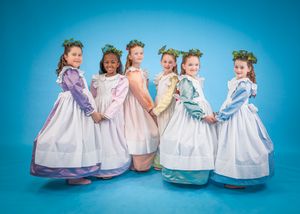 Children in matching white dresses and colorful sashes sit together on a blue background.