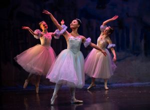 Ballet dancers in pink tutus perform graceful movements on a dark stage during a classical dance performance.