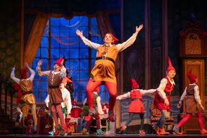 Performers in colorful costumes dance and gesture dramatically on an ornate theater stage during a musical production.