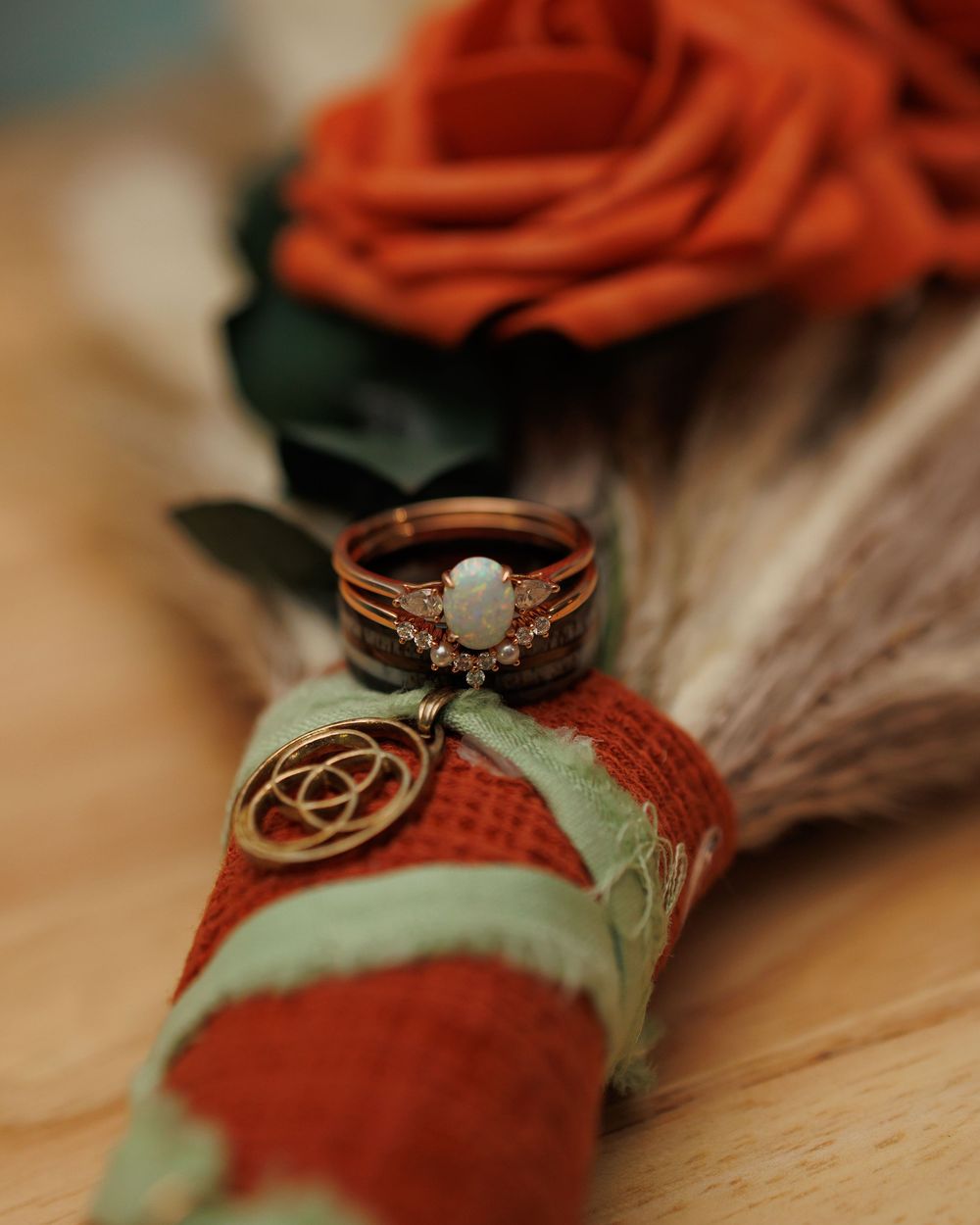 Rose gold engagement ring with opal stone displayed on red and green fabric with decorative charm and rose in background.