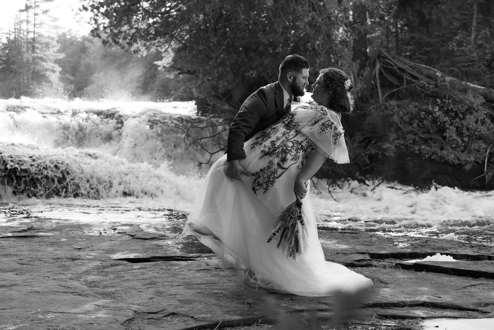 A romantic black and white wedding photo of a couple embracing by a misty waterfall.