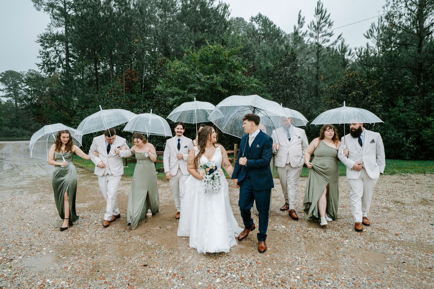 Wedding party in light colored attire walking and jumping along a beach path during a celebration.