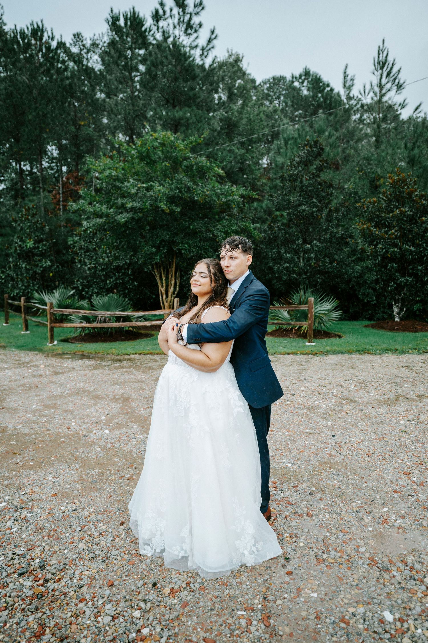 A couple embraces on their wedding day outdoors surrounded by tall pine trees and natural scenery.