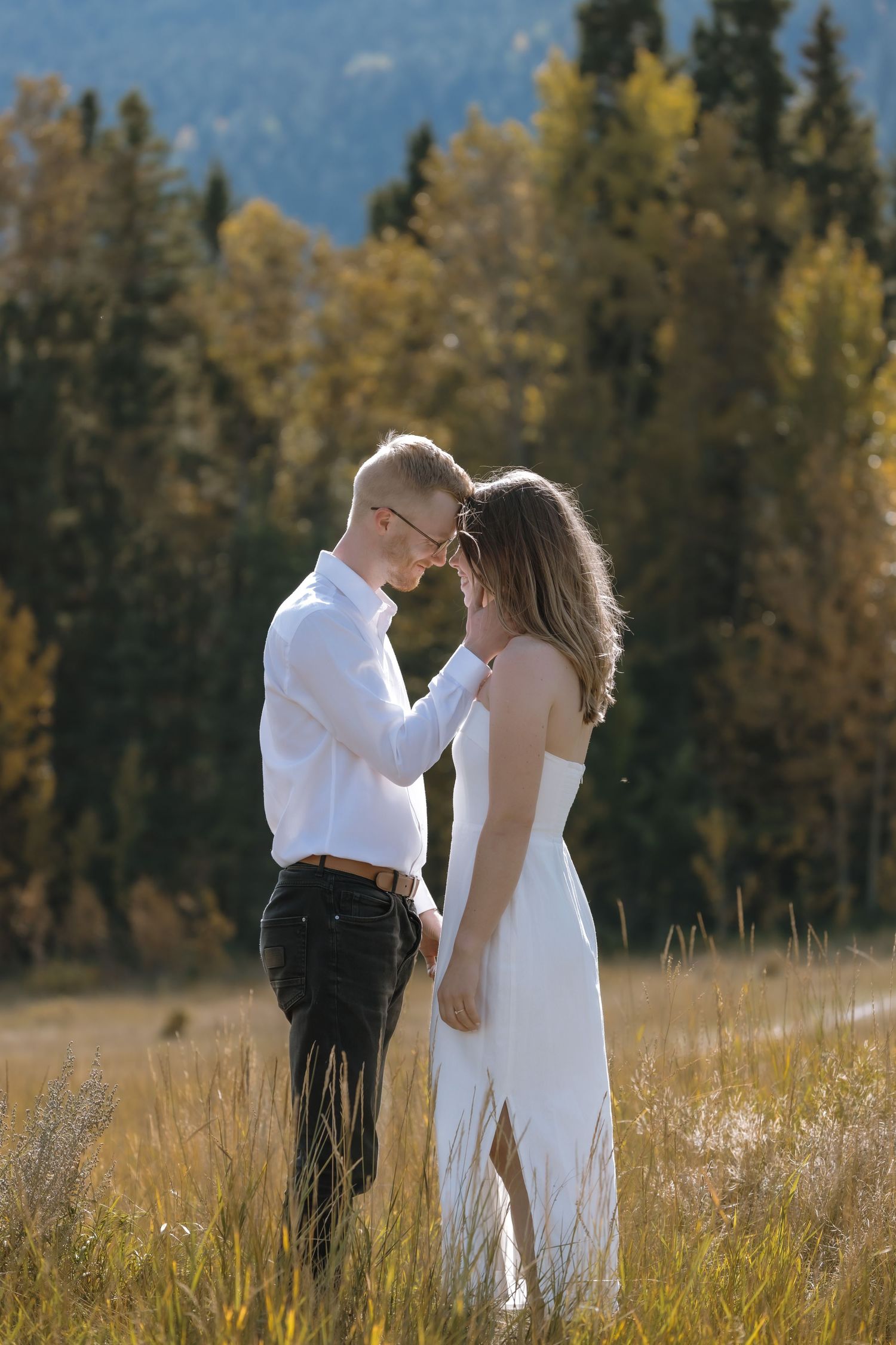 A couple shares an intimate moment in a mountain meadow with golden autumn trees in the background. Bismarck, ND photographer