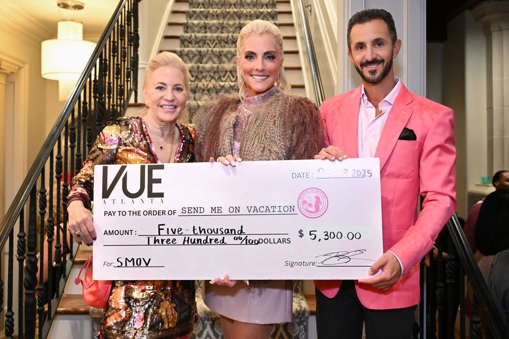 People holding large ceremonial checks at a charity event in an elegant indoor setting.