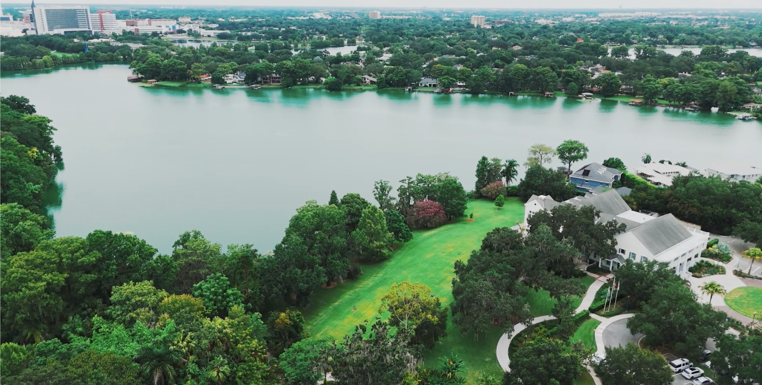 Aerial panoramic view of a waterfront city skyline with modern buildings and green spaces.