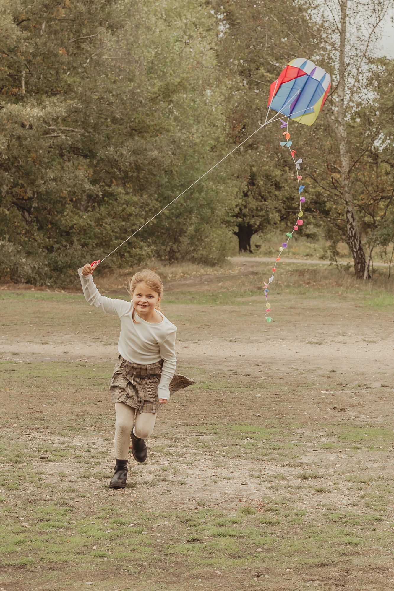 Child flying a colorful kite in an open field during autumn.