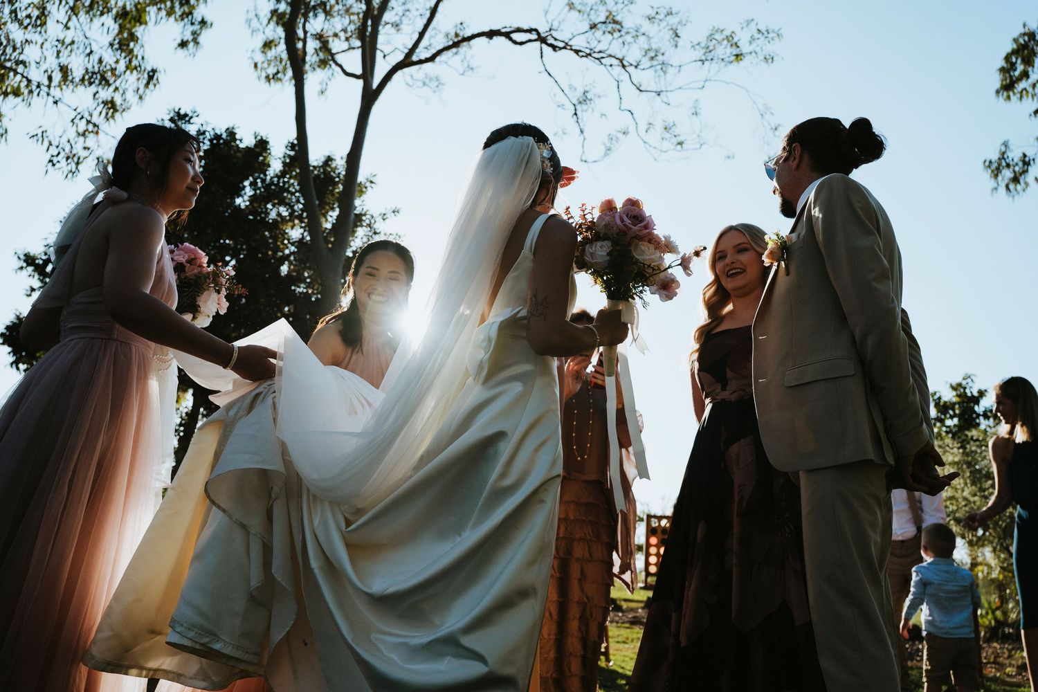 A wedding couple shares an intimate moment under sunlit trees during an outdoor ceremony.