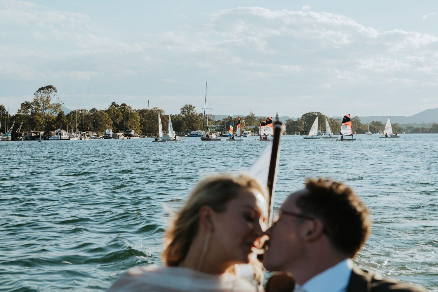 A wedding couple shares an intimate moment under sunlit trees during an outdoor ceremony.