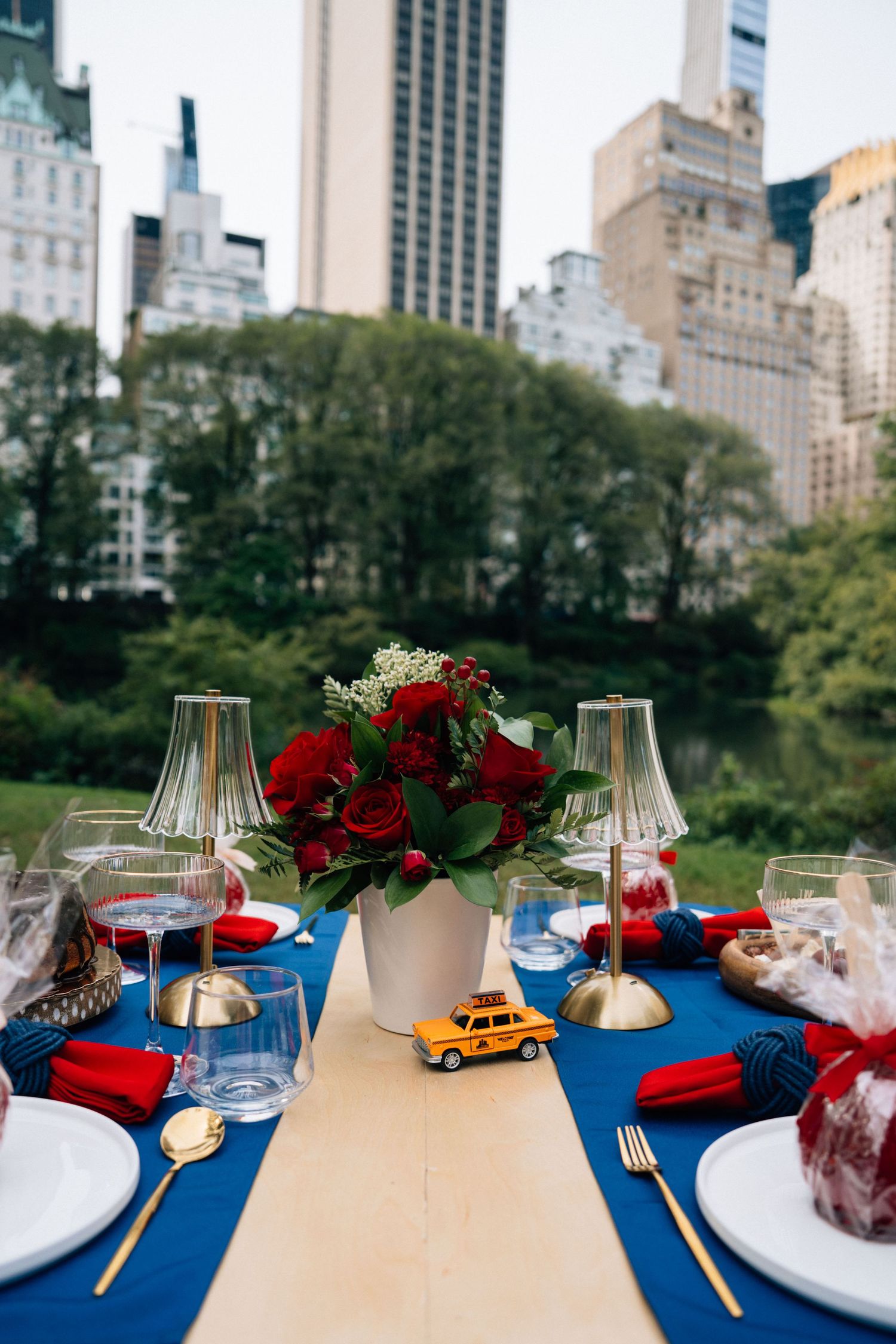 Elegant table setting with red roses and blue tablecloth overlooking New York City skyline and Central Park.