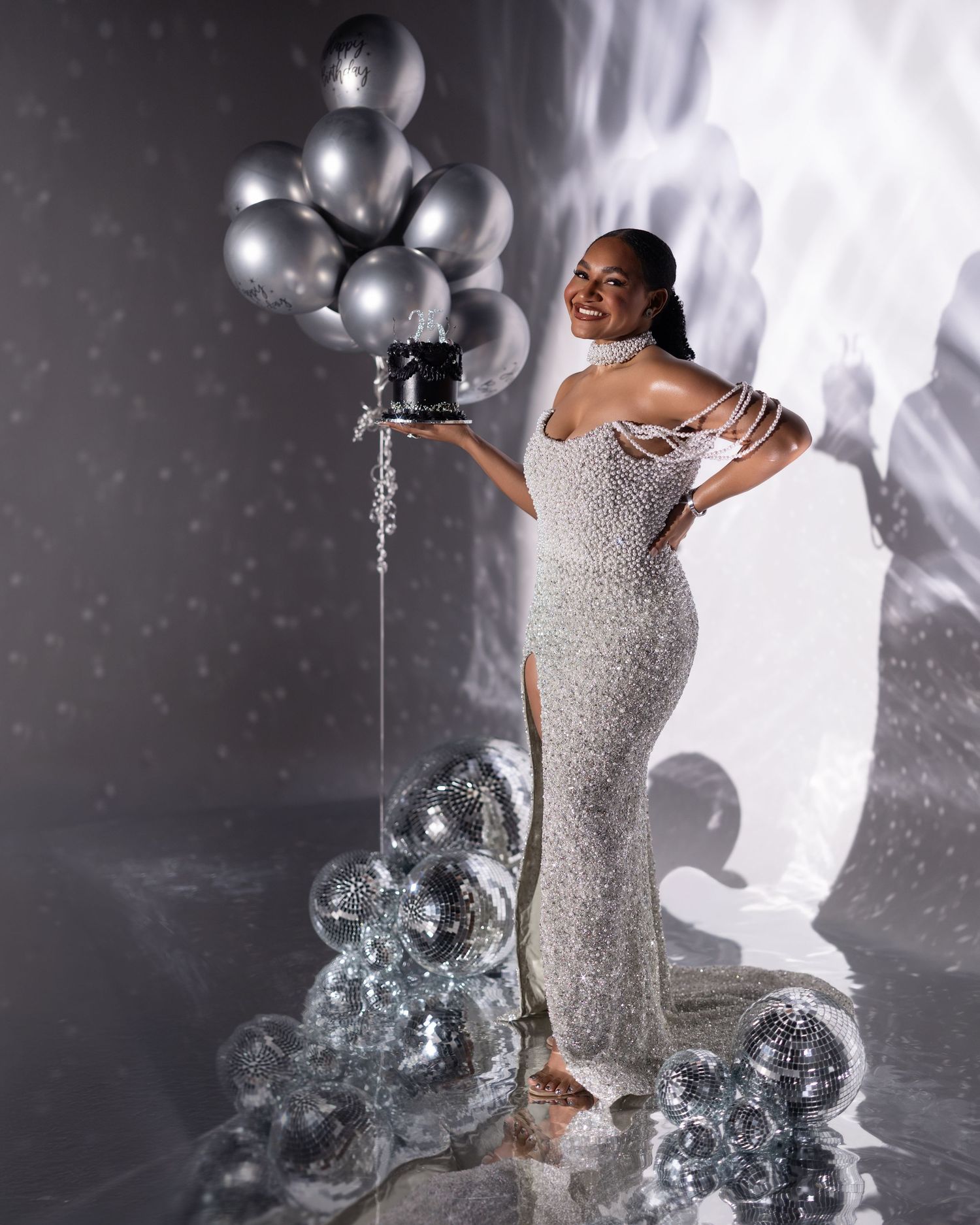 A glamorous silver sequin dress sparkles against a dark backdrop with disco balls and silver balloons creating a festive atmosphere.