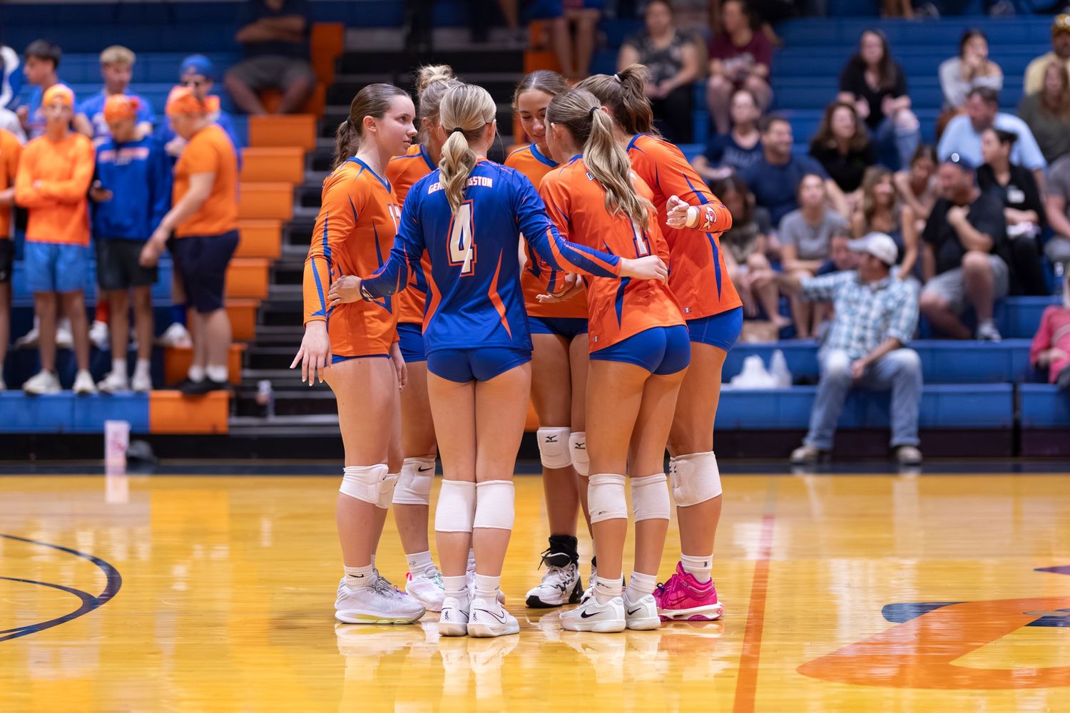 Volleyball team huddles together during a match on an indoor court.