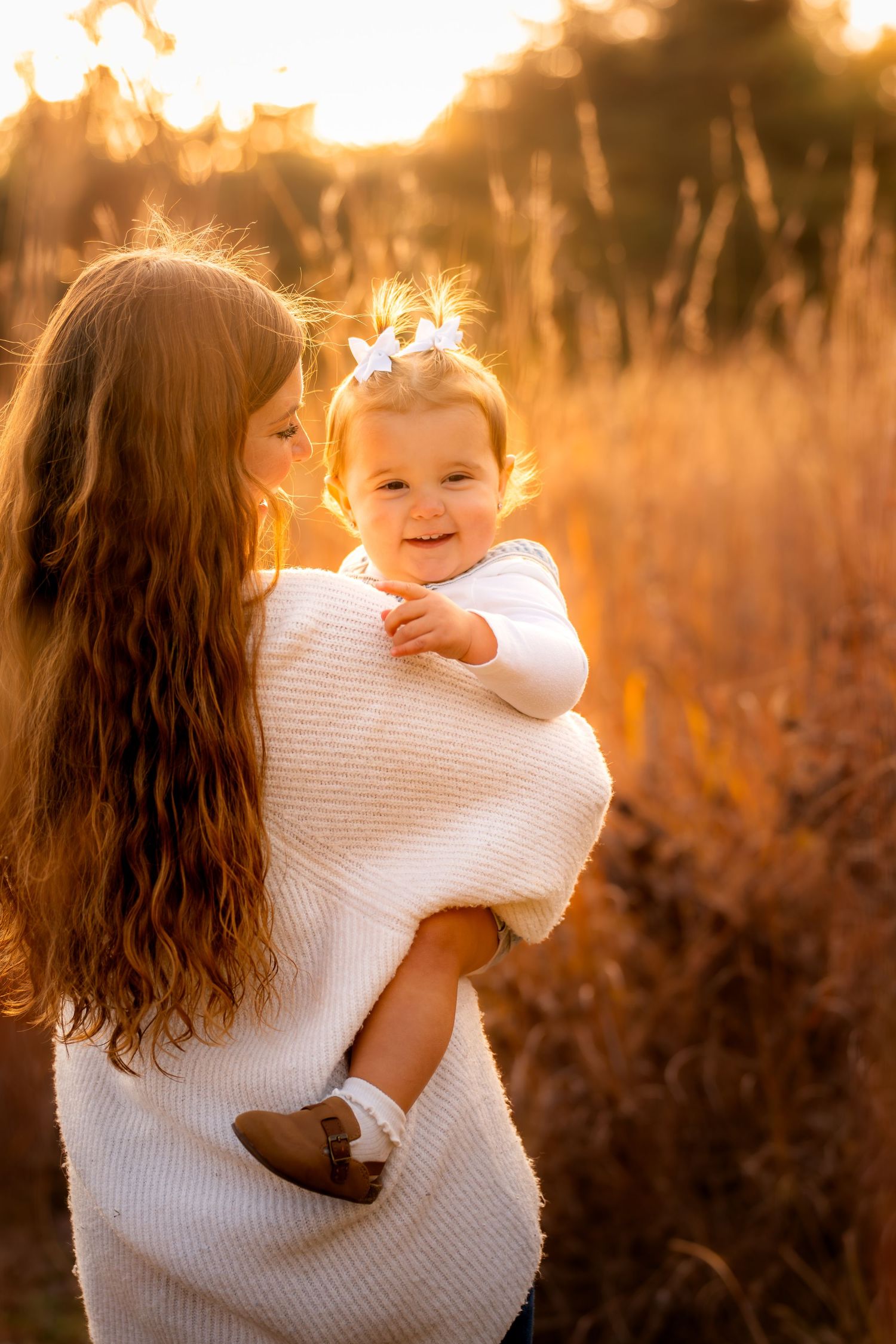 A tender moment captured at sunset as a mother holds her baby in a golden-lit field.