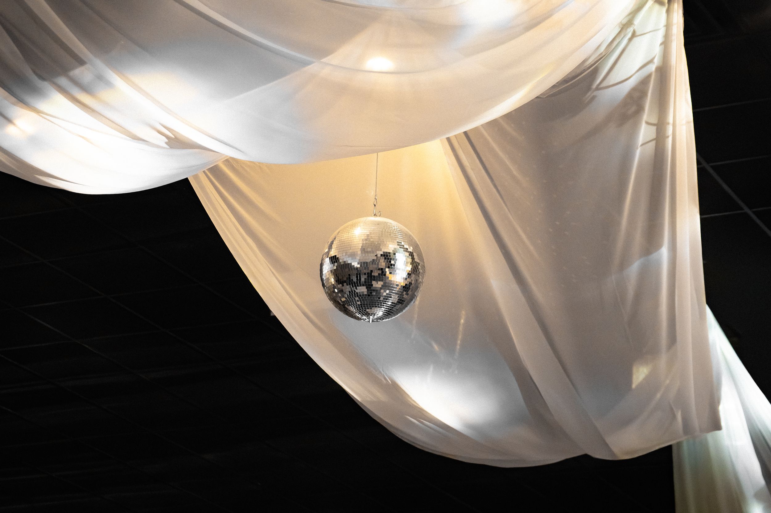 Disco ball hanging among white draped fabric creating an elegant party atmosphere.