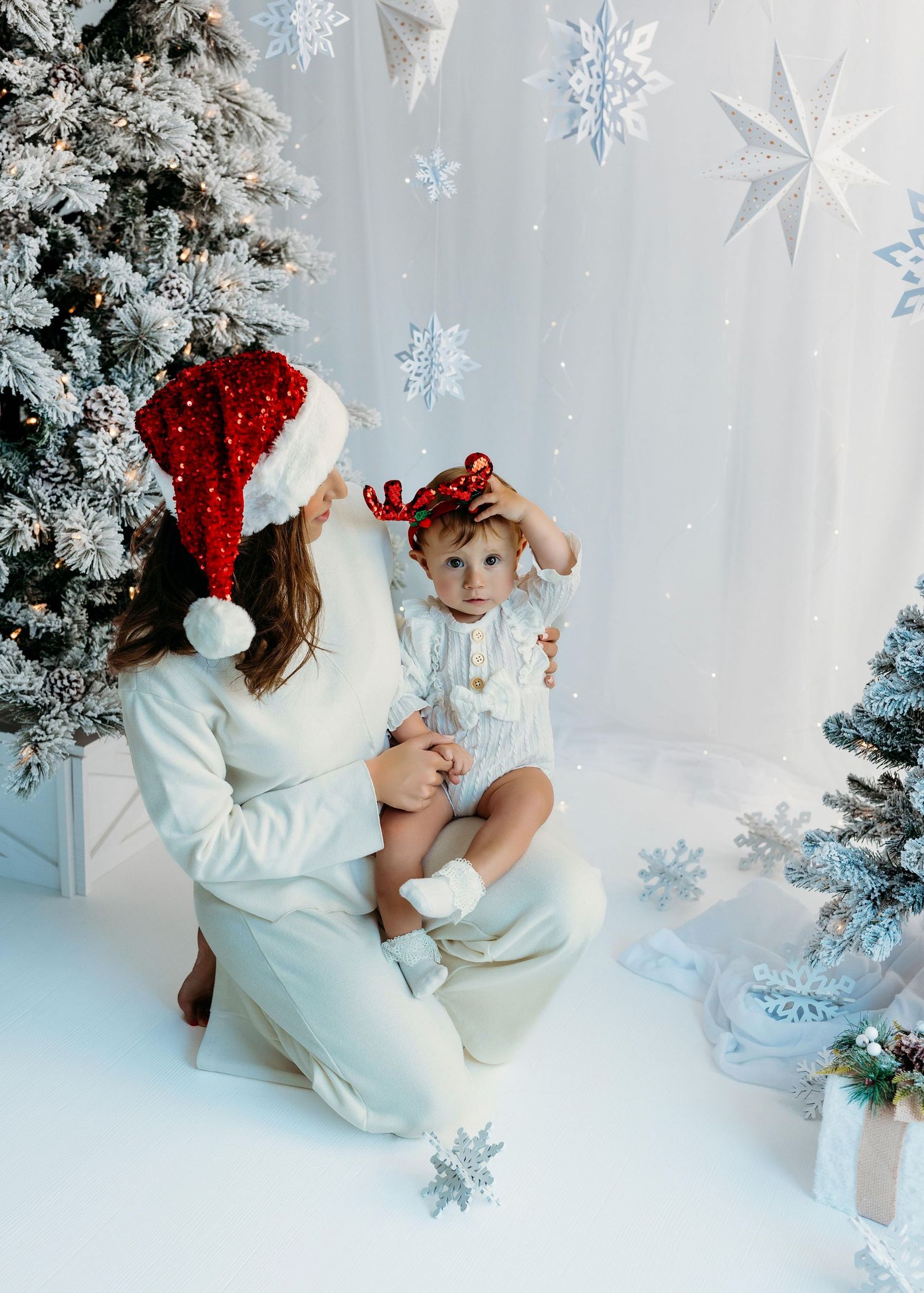 A festive winter scene with a decorated Christmas tree, snowflakes, and two figures in white against a snowy backdrop.