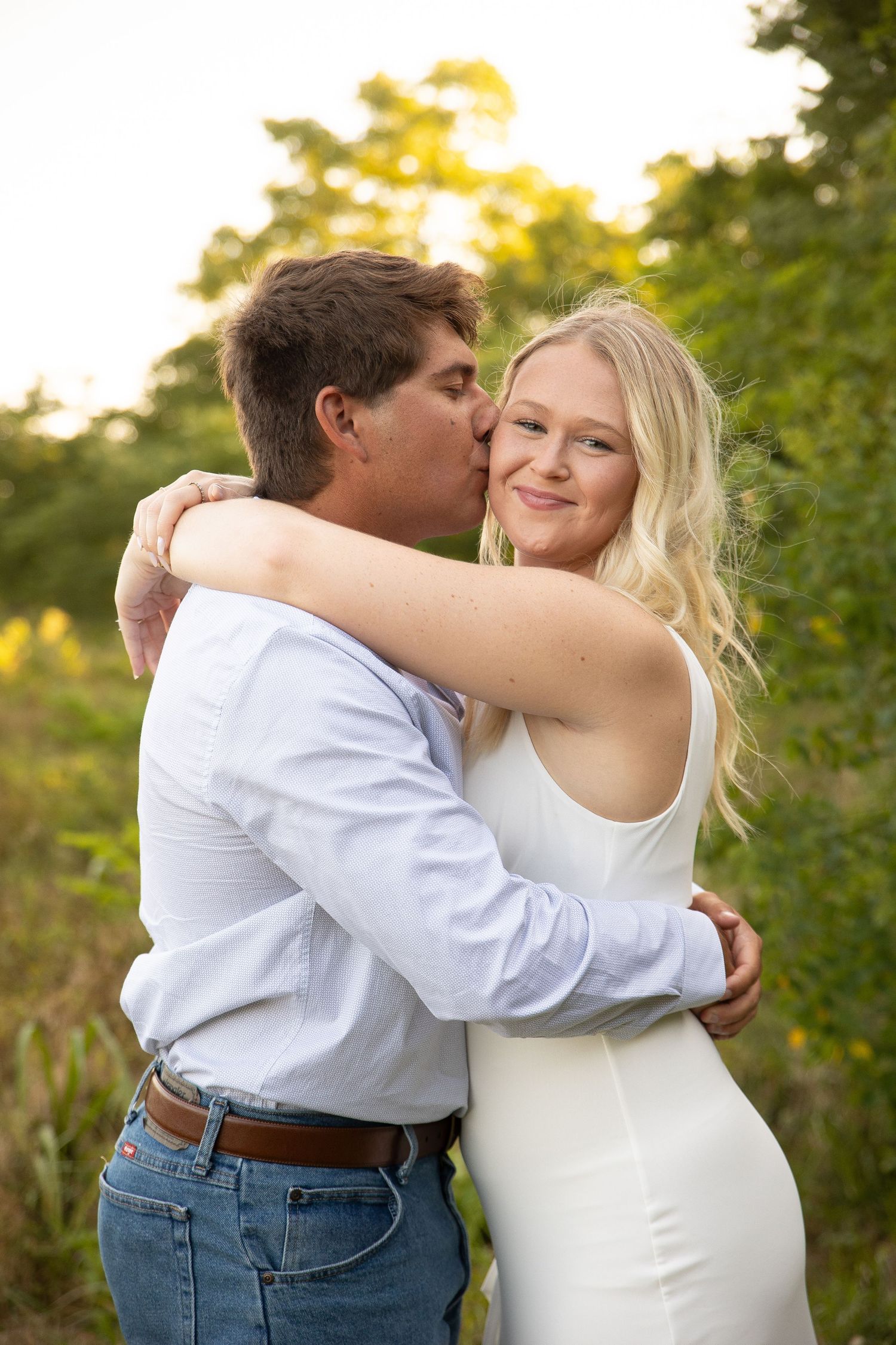 A romantic couple embraces outdoors during a golden sunset photoshoot in a garden setting.