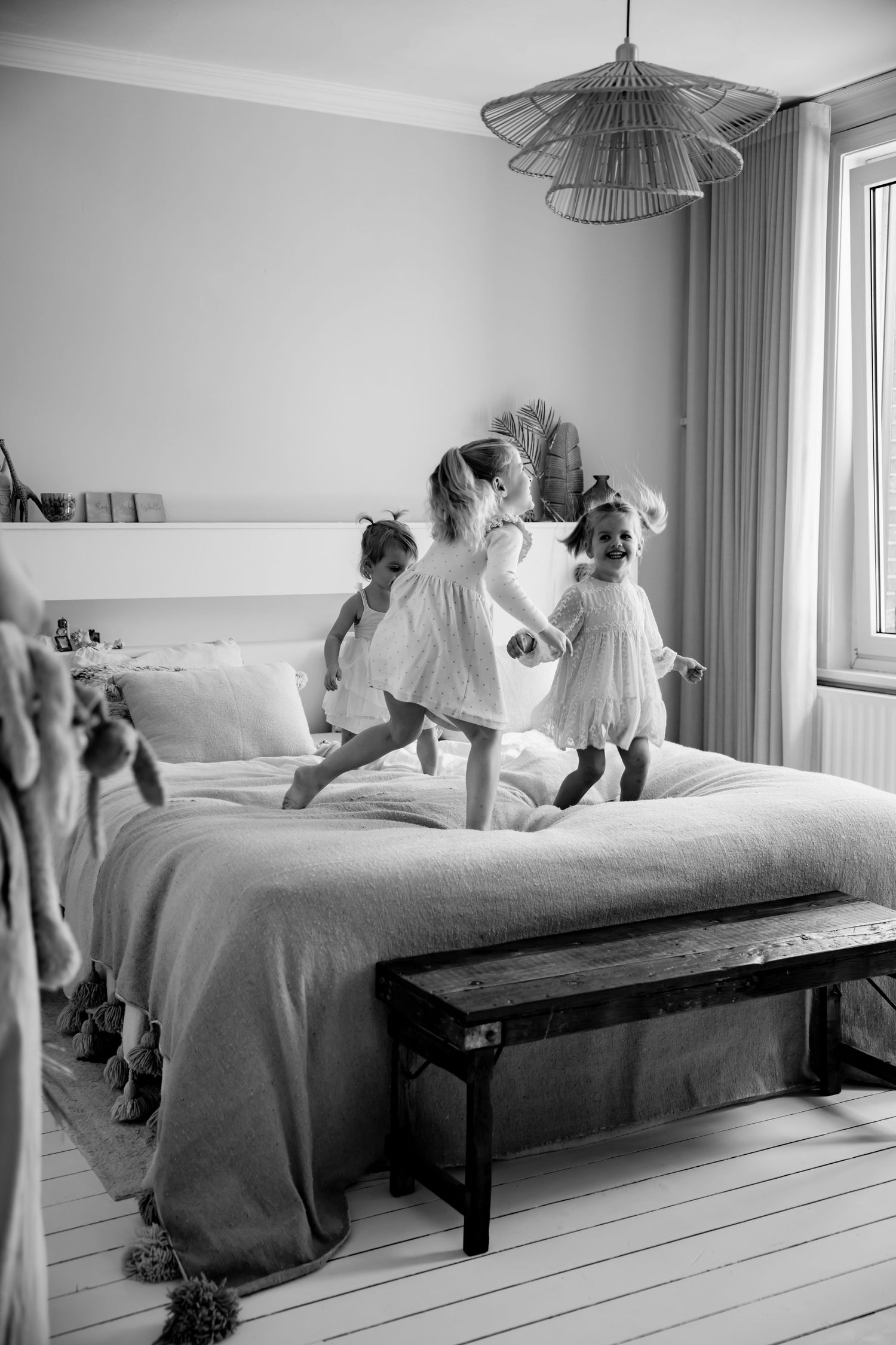 Children jumping and playing on a bed in a bright bedroom with modern decor.