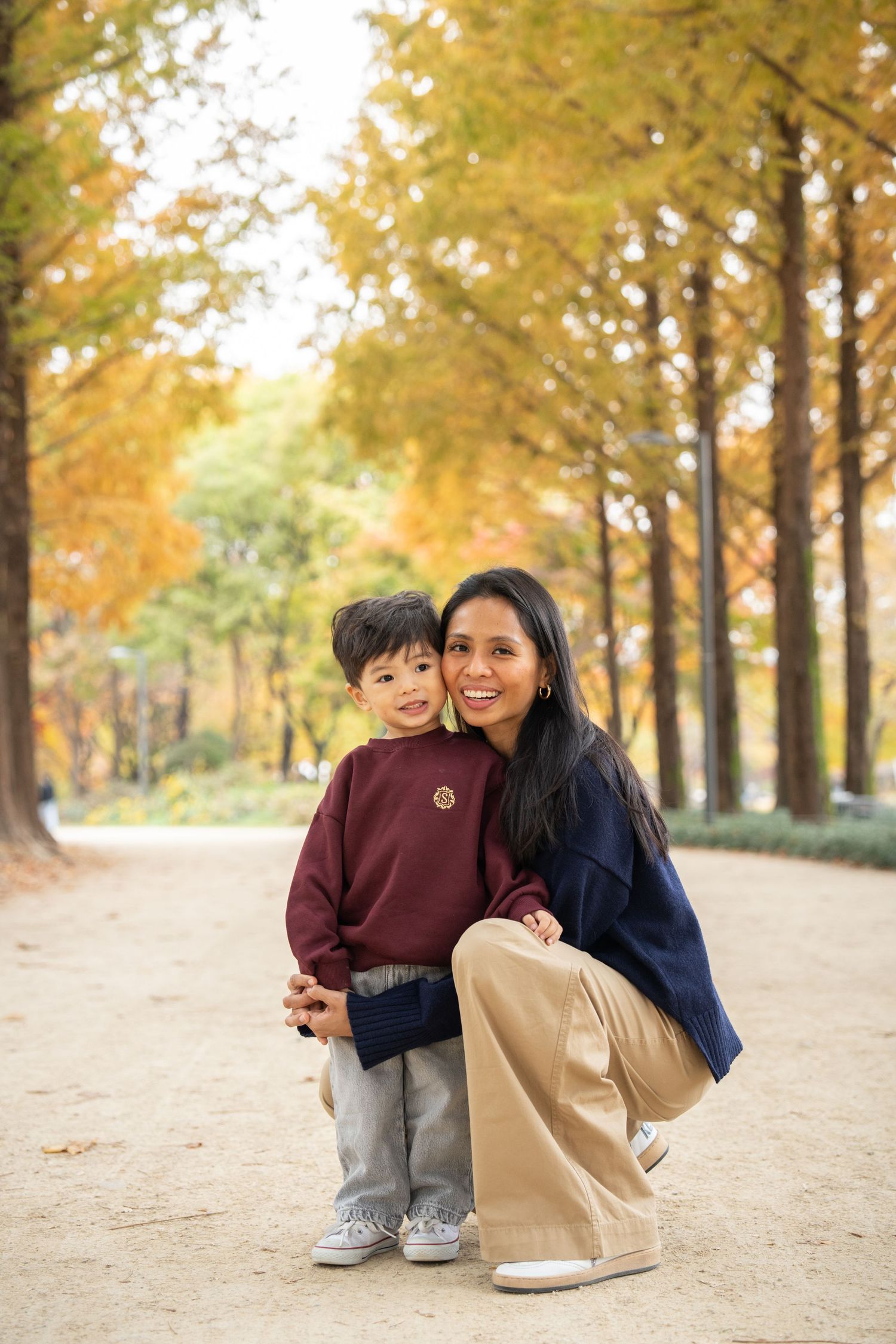Parent and child share a joyful moment among golden autumn trees on a path lined with fallen leaves.