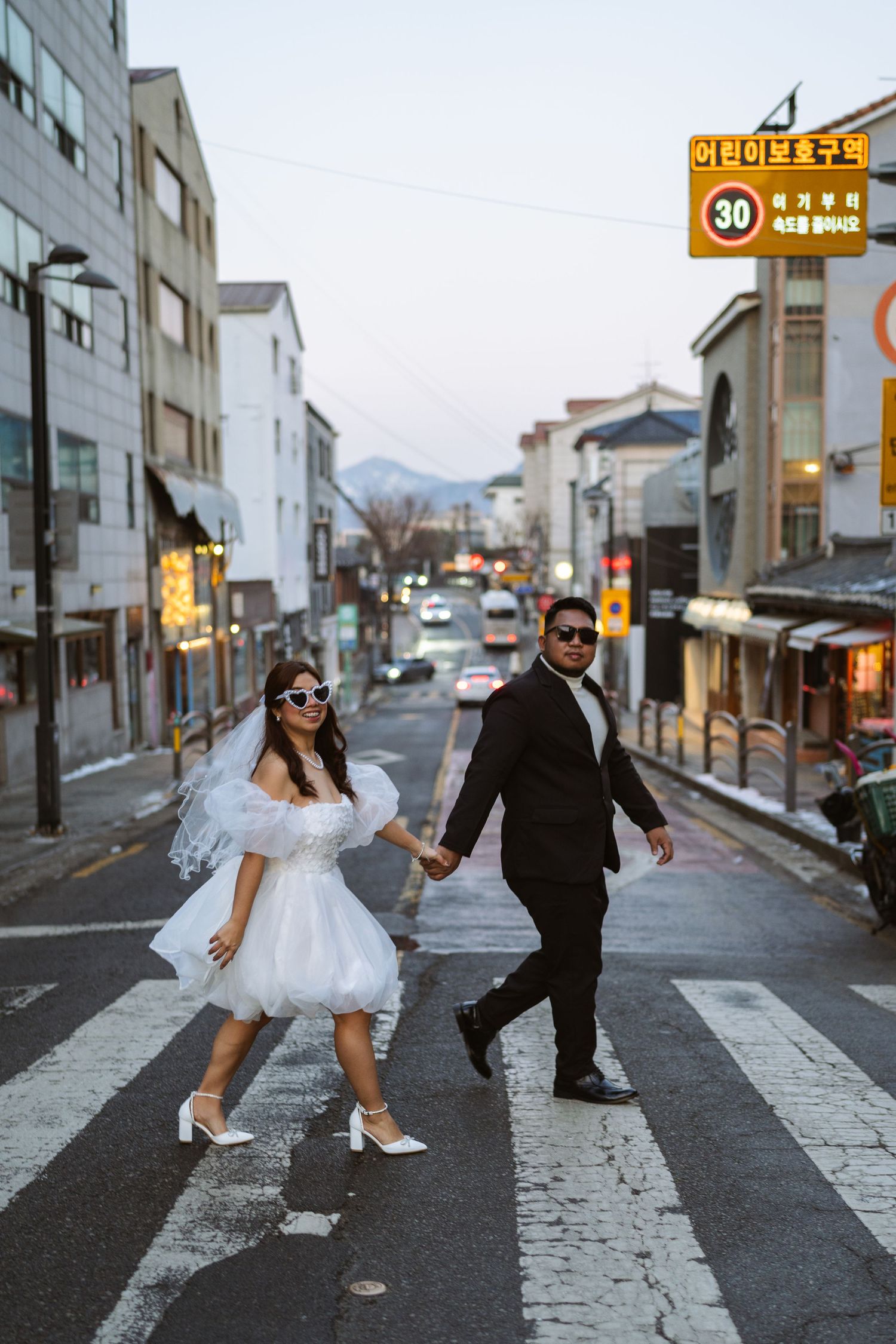 A couple in wedding attire poses playfully on a street in a series of four connected photos.