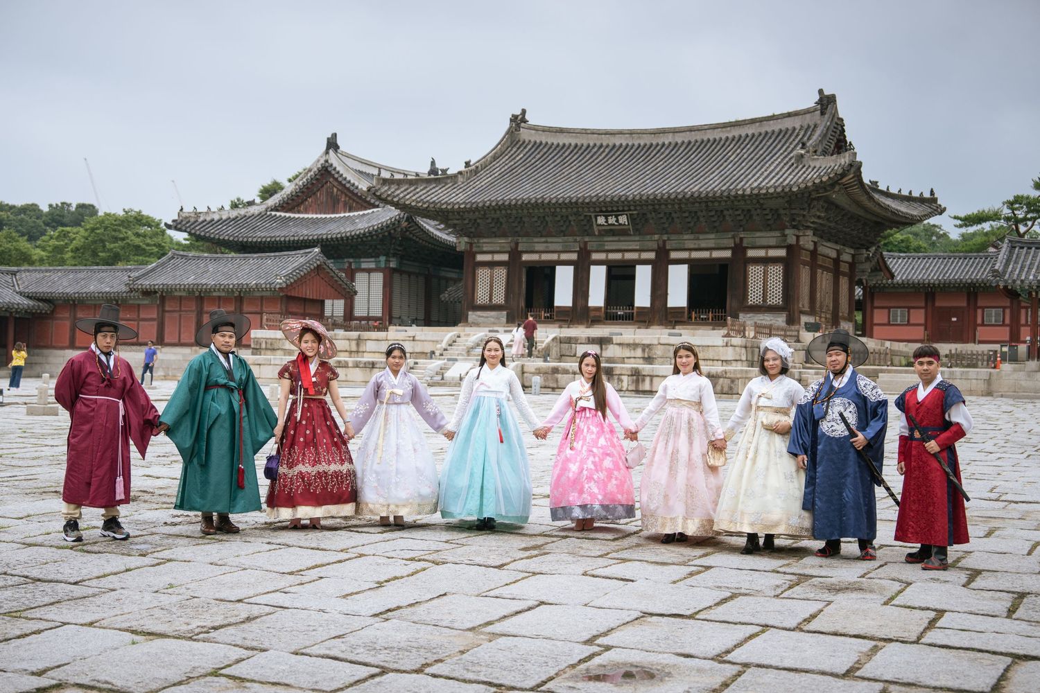 People wearing colorful traditional Korean hanbok dresses walk through a historic palace courtyard in Seoul.
