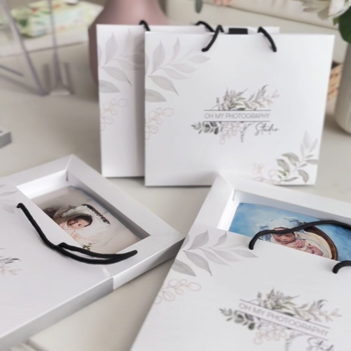 Elegant white photo delivery boxes with floral designs and black ribbons.