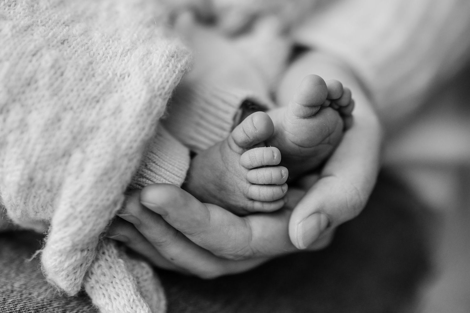 Black and white detail shot of baby feet wrapped in knit blanket.