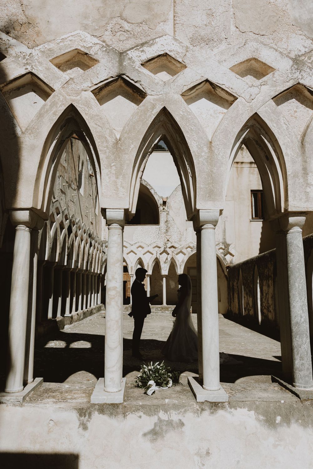 Gothic stone archways and columns in a historic cloister create dramatic shadows and architectural details.